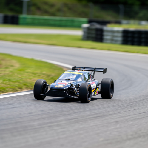 Petite voiture de course télécommandée électrique au 1/10 en pleine accélération sur une piste de touring, à la lumière du jour, avec un effet de mouvement et un arrière-plan de circuit.